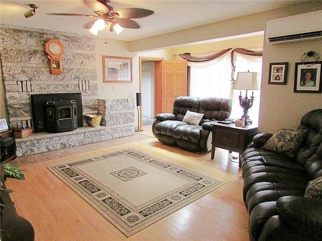 living room featuring an AC wall unit, light hardwood / wood-style flooring, a wood stove, and ceiling fan