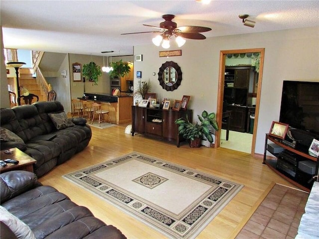 living area with light wood-style flooring, a ceiling fan, and stairs