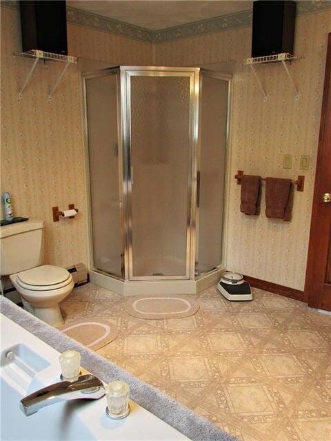 bathroom with toilet, a shower stall, and wallpapered walls