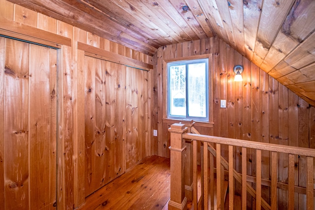 hallway with wood-type flooring, lofted ceiling, and wood walls