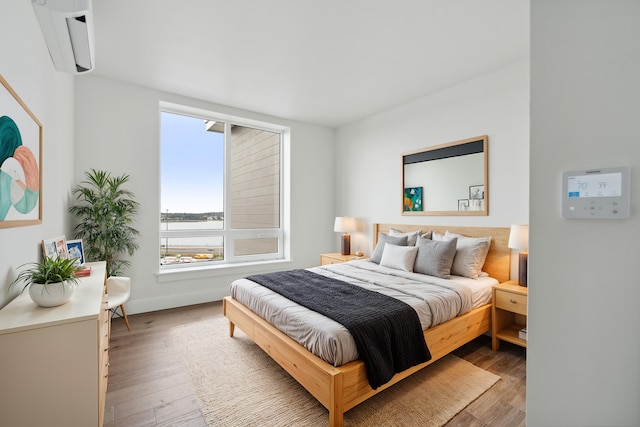 bedroom with an AC wall unit, a water view, and wood-type flooring