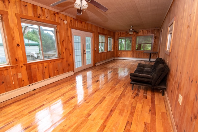 unfurnished room with ceiling fan, wooden walls, light hardwood / wood-style flooring, and a baseboard heating unit