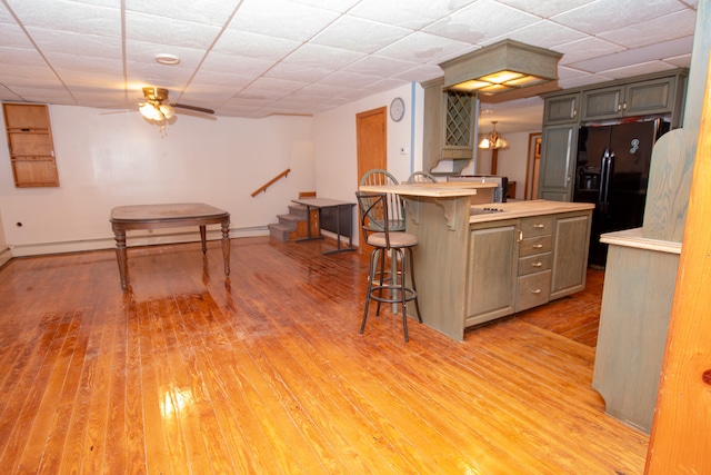 kitchen with light wood-type flooring, ceiling fan with notable chandelier, a kitchen island, black fridge with ice dispenser, and a kitchen breakfast bar