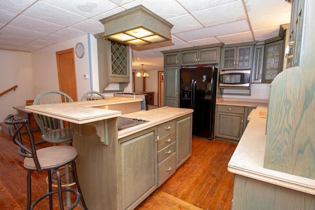 kitchen featuring light wood-type flooring, gray cabinets, a center island, black fridge with ice dispenser, and a kitchen bar