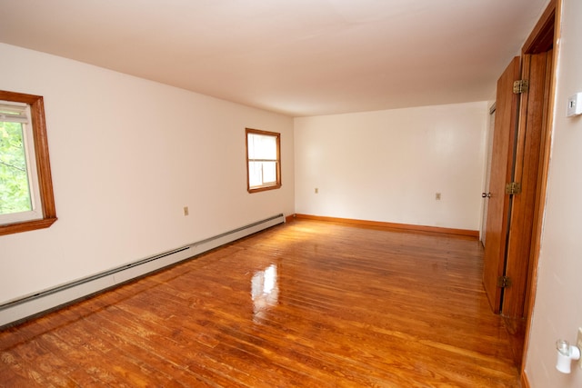 empty room with light wood-type flooring, a baseboard heating unit, and a wealth of natural light