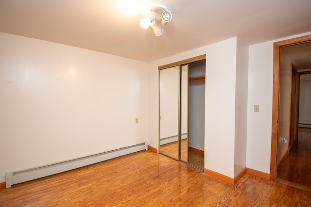 unfurnished bedroom featuring hardwood / wood-style floors, a closet, and a baseboard heating unit