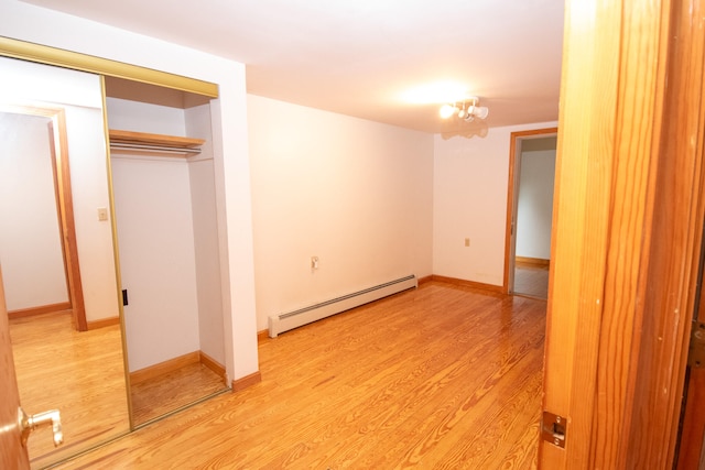 unfurnished bedroom featuring a closet, light hardwood / wood-style floors, and a baseboard heating unit