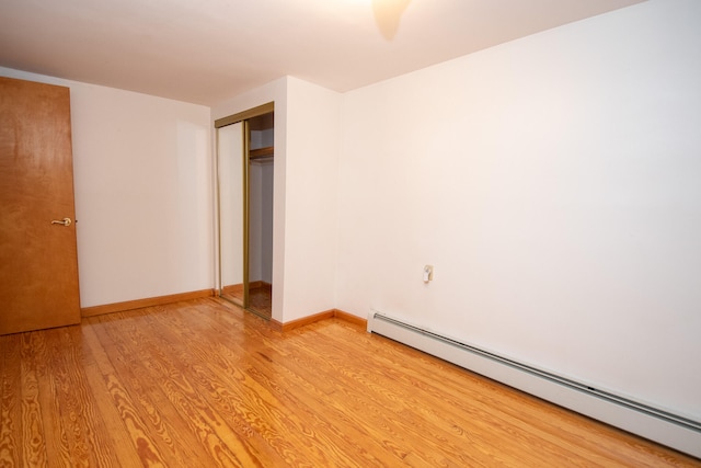 unfurnished bedroom with light wood-type flooring, a closet, and a baseboard heating unit