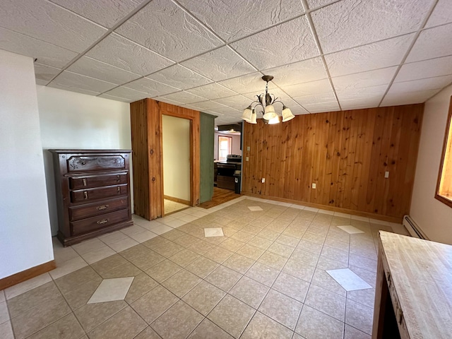 unfurnished dining area featuring light tile patterned floors, wooden walls, a chandelier, and baseboard heating