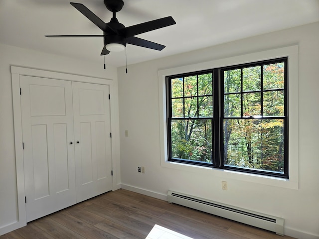 unfurnished bedroom featuring multiple windows, ceiling fan, a baseboard radiator, and wood-type flooring