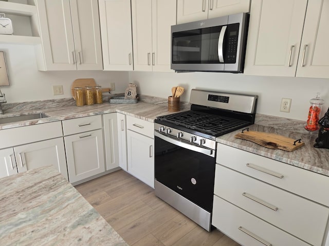 kitchen with sink, light stone countertops, white cabinetry, light wood-type flooring, and appliances with stainless steel finishes