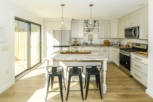 kitchen with light wood-type flooring, hanging light fixtures, light stone counters, and stainless steel appliances