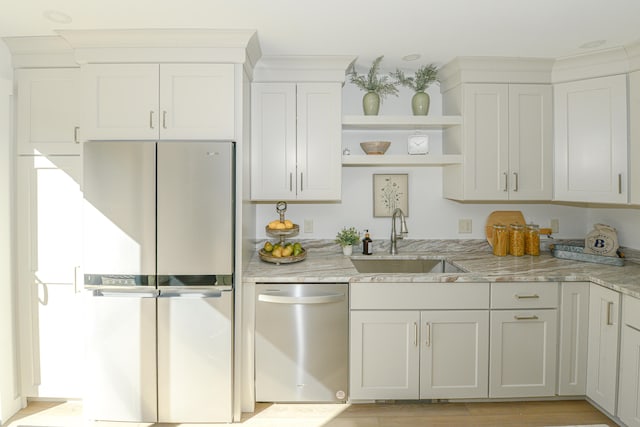 kitchen featuring stainless steel appliances, sink, light stone countertops, white cabinetry, and light wood-type flooring