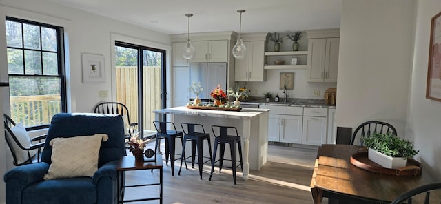 kitchen with stainless steel refrigerator, hanging light fixtures, sink, light hardwood / wood-style floors, and white cabinets