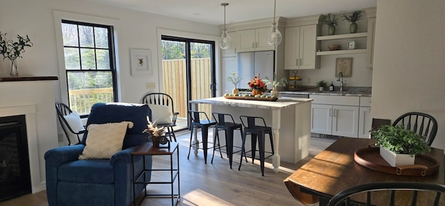 kitchen with stainless steel fridge, pendant lighting, sink, white cabinets, and light hardwood / wood-style flooring