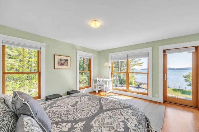 bedroom with a water view, access to outside, light wood-type flooring, and multiple windows