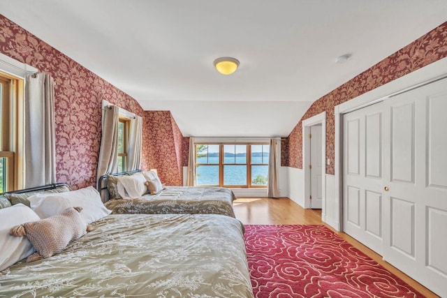 bedroom with a water view, vaulted ceiling, and light hardwood / wood-style flooring