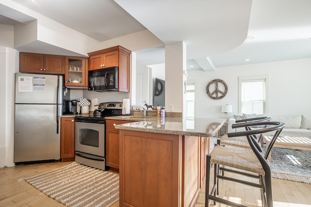 kitchen with light stone counters, stainless steel appliances, sink, kitchen peninsula, and light hardwood / wood-style flooring