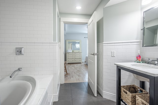 bathroom with a bathtub, sink, tile patterned flooring, and tile walls