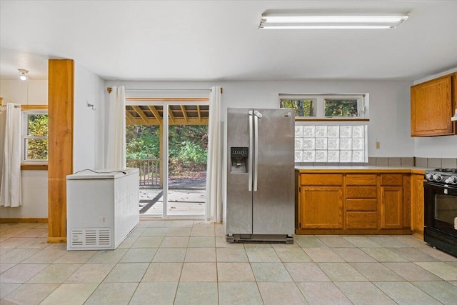 kitchen with black range, light tile patterned floors, stainless steel fridge with ice dispenser, and a wealth of natural light