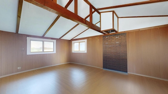 empty room with wood walls, baseboards, wood finished floors, and lofted ceiling with beams