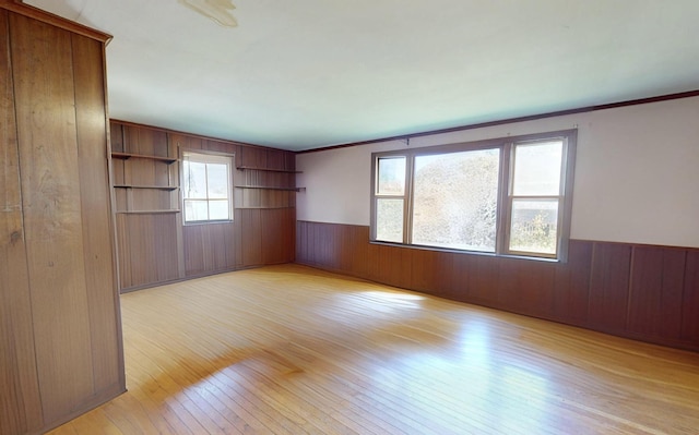 spare room featuring wood walls, light wood finished floors, ornamental molding, and a wainscoted wall