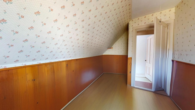 additional living space featuring wainscoting, light wood-style flooring, wallpapered walls, and lofted ceiling