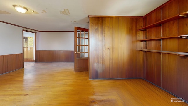 empty room featuring parquet floors, crown molding, wooden walls, and wainscoting