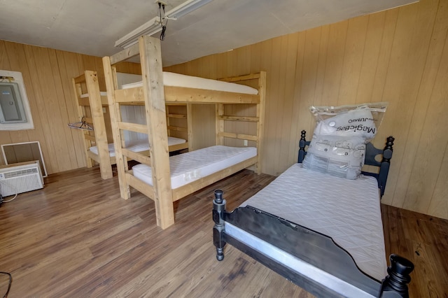 bedroom with electric panel, wood walls, hardwood / wood-style floors, and a wall mounted AC