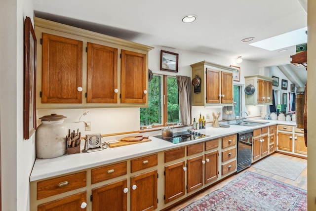 kitchen featuring vaulted ceiling with skylight, brown cabinetry, black appliances, a sink, and light countertops
