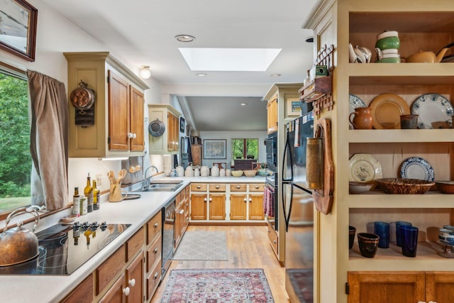 kitchen with light countertops, black appliances, light wood-style floors, a skylight, and a sink