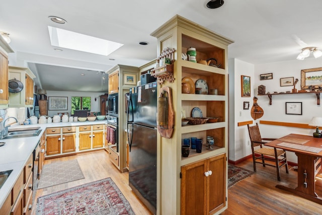 kitchen with light wood-style floors, black appliances, a skylight, light countertops, and a sink