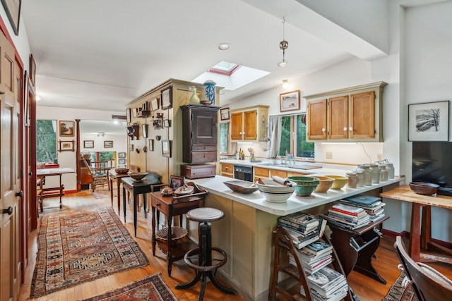 kitchen with light countertops, a breakfast bar, light wood-type flooring, a peninsula, and a skylight