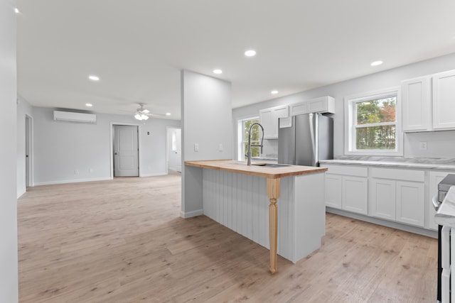 kitchen featuring butcher block countertops, stainless steel refrigerator, a wall mounted air conditioner, and white cabinetry