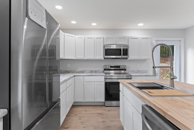 kitchen featuring appliances with stainless steel finishes, light wood-type flooring, white cabinetry, and sink