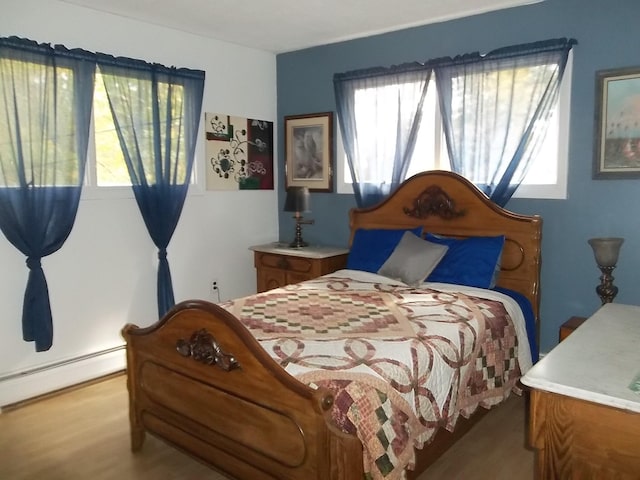 bedroom with a baseboard heating unit and light hardwood / wood-style floors