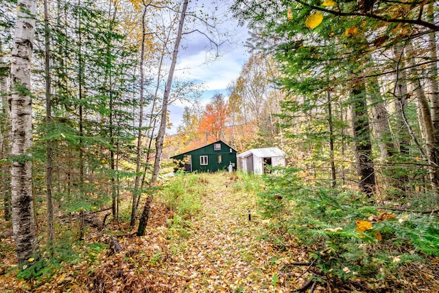 view of yard with a storage shed, a view of trees, and an outbuilding