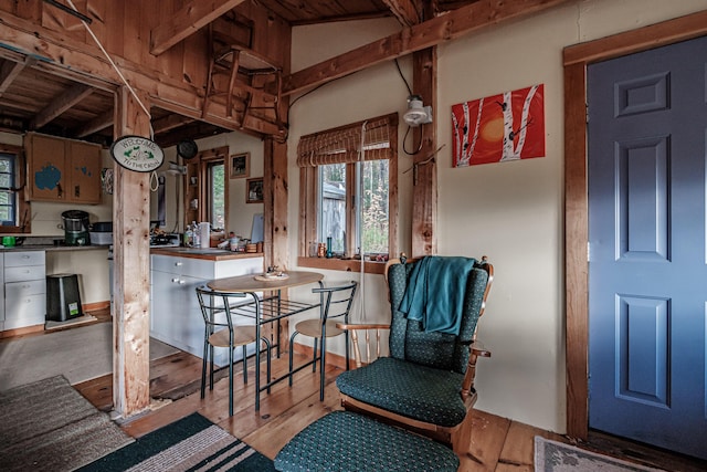 dining space featuring wood finished floors and vaulted ceiling with beams