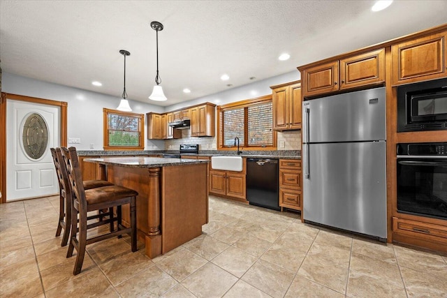 kitchen featuring tasteful backsplash, a kitchen island, black appliances, pendant lighting, and sink