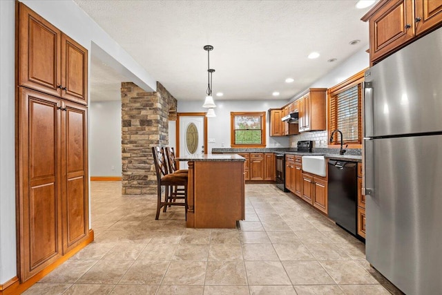 kitchen with a kitchen island, a kitchen breakfast bar, hanging light fixtures, black appliances, and decorative columns