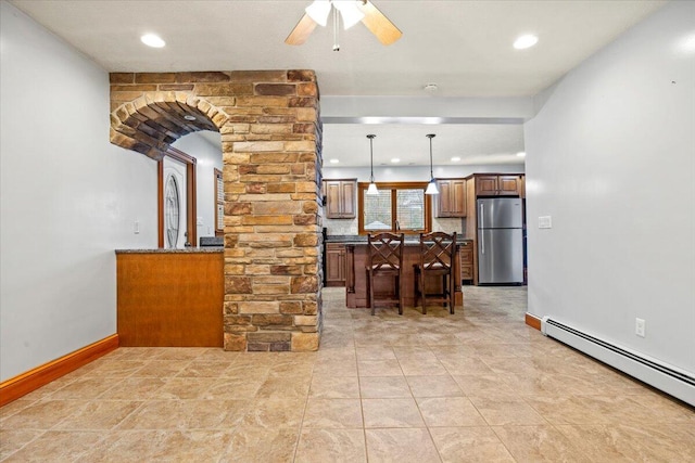 kitchen featuring a breakfast bar, decorative columns, stainless steel refrigerator, pendant lighting, and baseboard heating