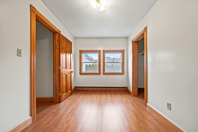 interior space with a baseboard heating unit, a textured ceiling, and light hardwood / wood-style floors