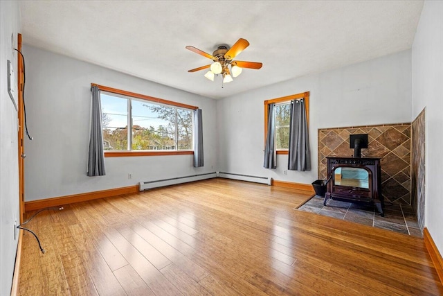 unfurnished living room featuring hardwood / wood-style flooring, a healthy amount of sunlight, a wood stove, and ceiling fan