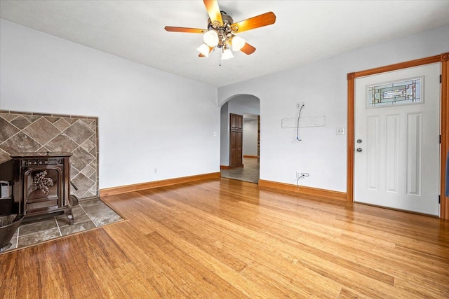 unfurnished living room with ceiling fan, hardwood / wood-style flooring, and a wood stove