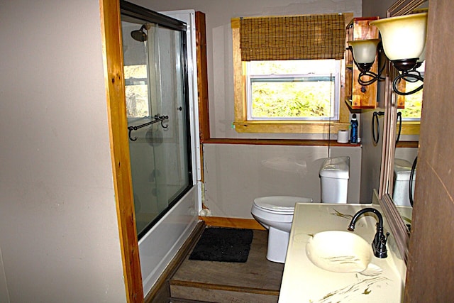 full bathroom featuring toilet, wood finished floors, vanity, bath / shower combo with glass door, and baseboards