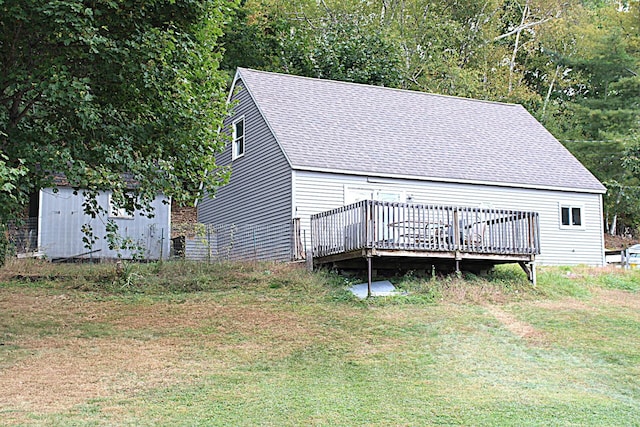 exterior space featuring a lawn, an outdoor structure, a deck, roof with shingles, and a storage shed