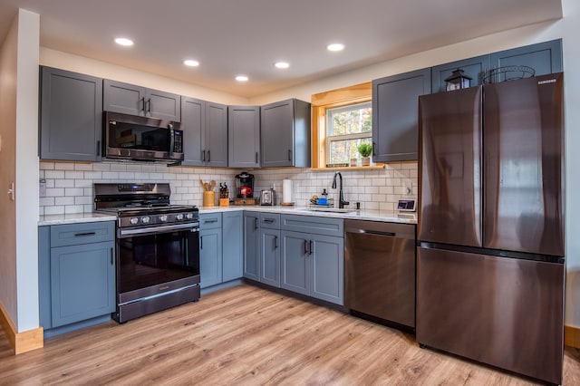 kitchen with light stone countertops, sink, tasteful backsplash, appliances with stainless steel finishes, and light wood-type flooring