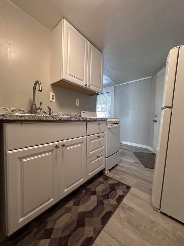 kitchen featuring white appliances, light wood-type flooring, light stone countertops, white cabinets, and sink