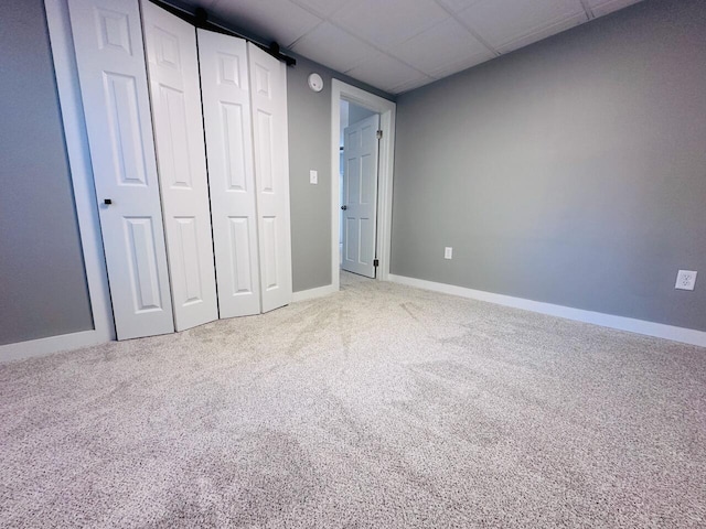 unfurnished bedroom with carpet floors, a closet, baseboards, and a drop ceiling