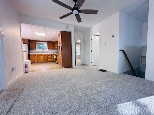 interior space with light colored carpet, a sink, baseboards, freestanding refrigerator, and brown cabinets